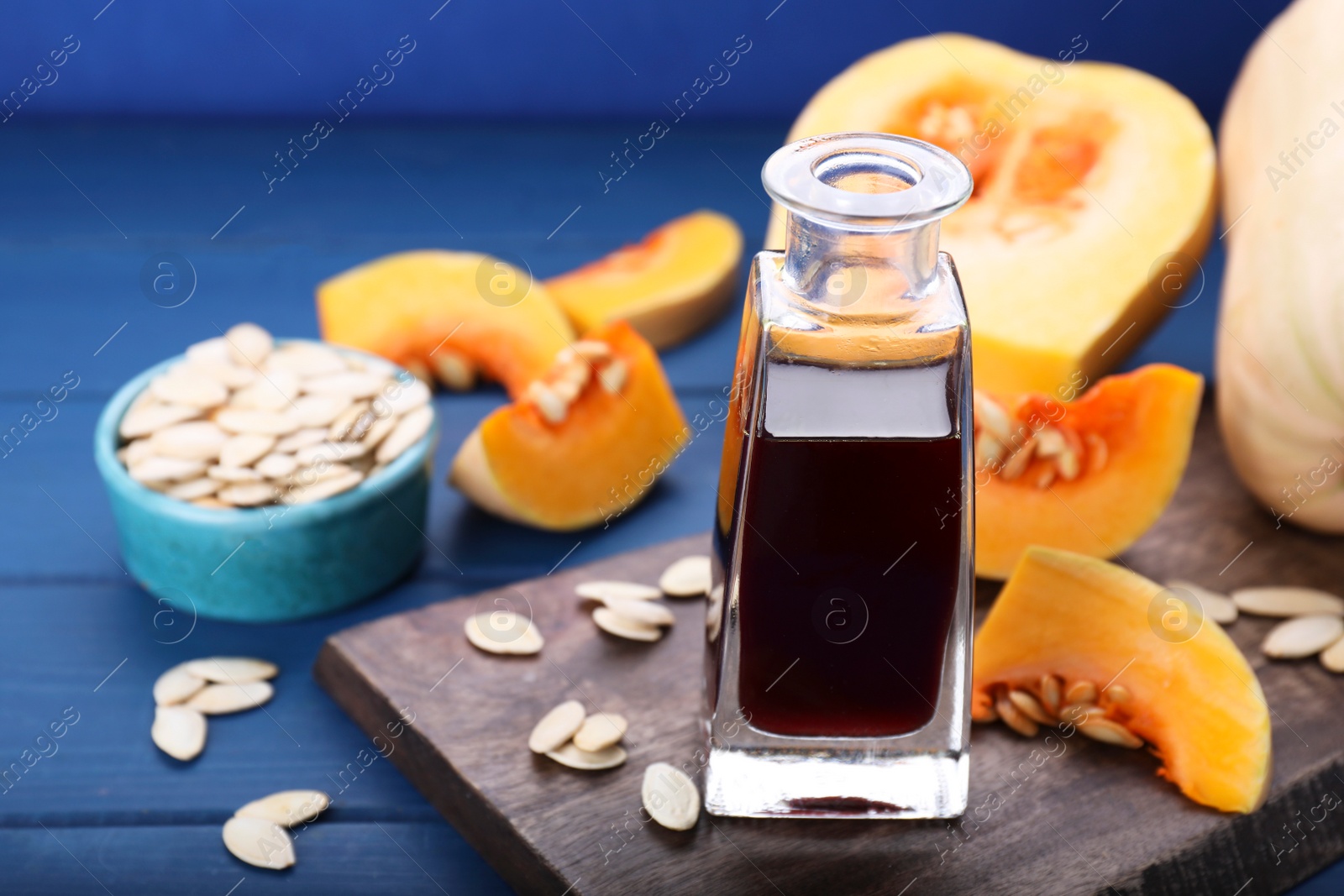 Photo of Fresh pumpkin seed oil in glass bottle on blue wooden table. Space for text