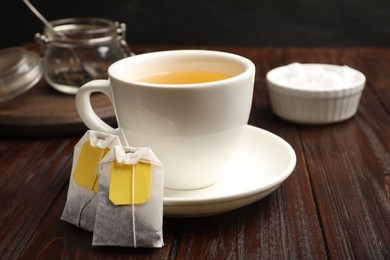 Photo of Tea bags and cup of hot beverage on wooden table, closeup