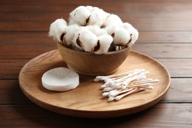 Plate with cotton swabs, pads and flowers on wooden background