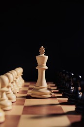 Photo of White king among pawns on chessboard against black background. Competition concept