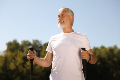 Senior man practicing Nordic walking with poles outdoors on sunny day