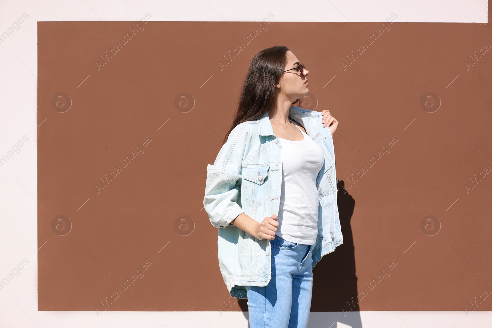 Photo of Young hipster woman in stylish jeans and jacket posing near color wall
