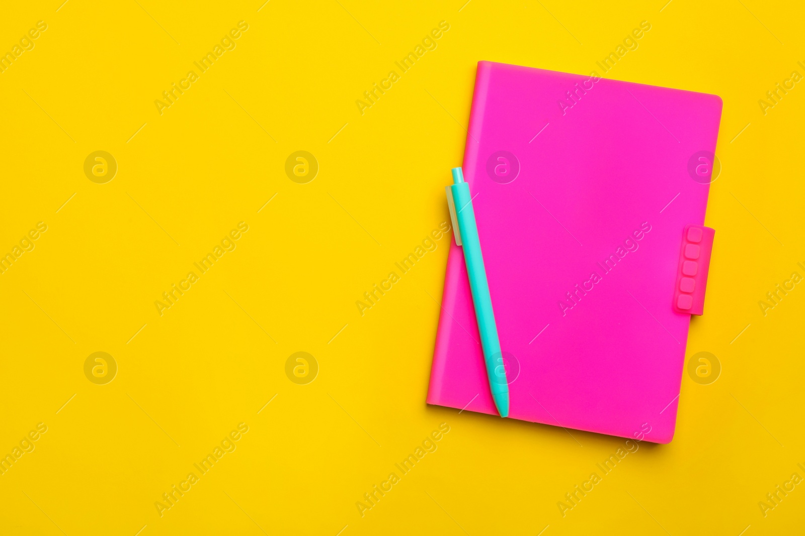 Photo of Pink notebook and pen on yellow background, top view. Space for text