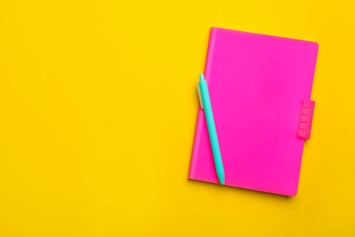 Photo of Pink notebook and pen on yellow background, top view. Space for text
