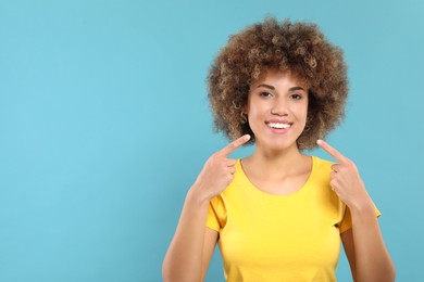 Woman showing her clean teeth and smiling on light blue background, space for text