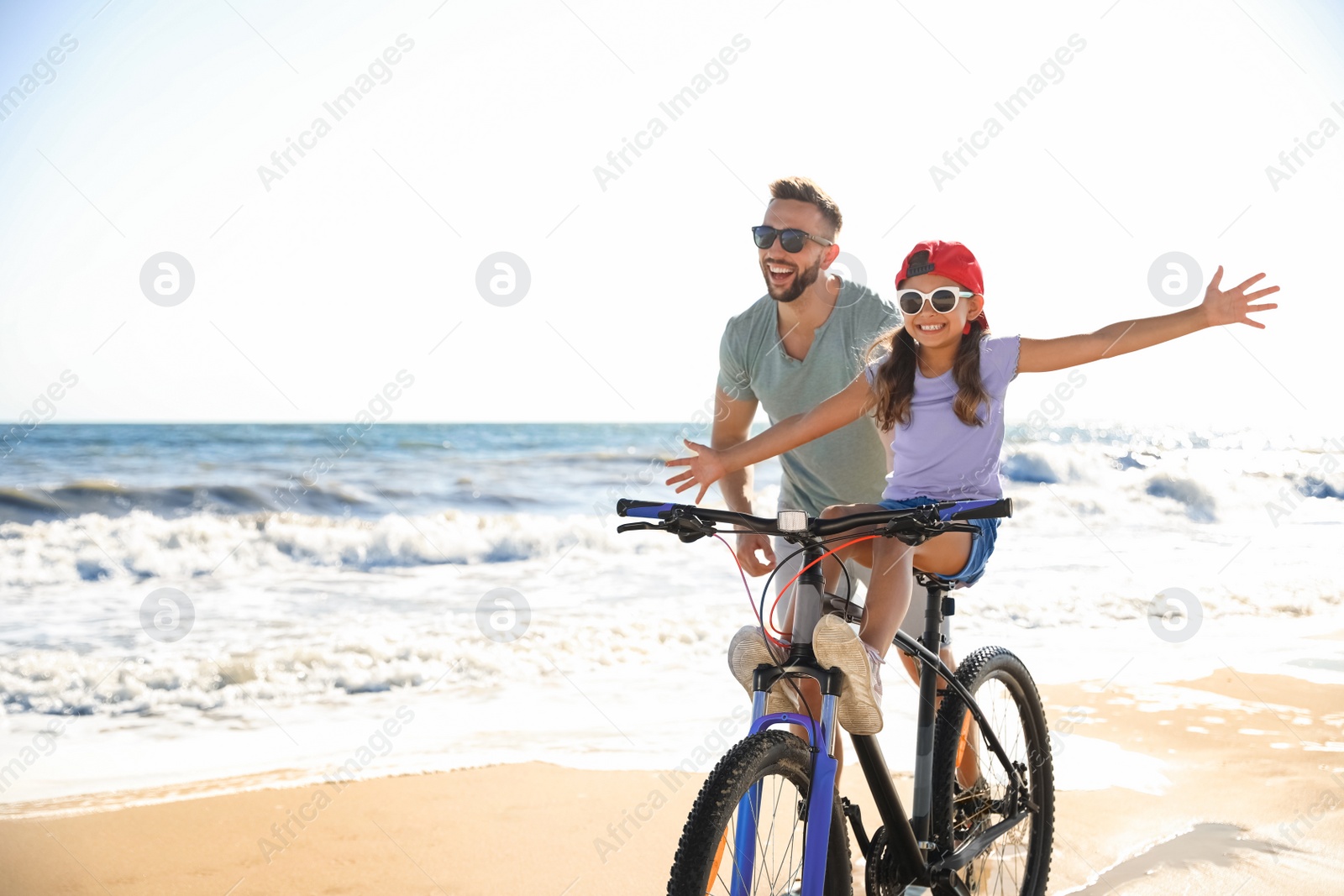 Photo of Happy father teaching daughter to ride bicycle on sandy beach near sea