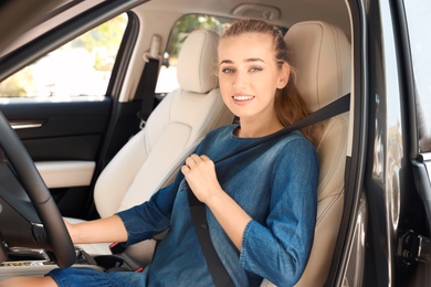 Photo of Female driver fastening safety belt in car