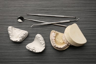 Photo of Dental models with gums and dentist tools on grey wooden table, flat lay. Cast of teeth