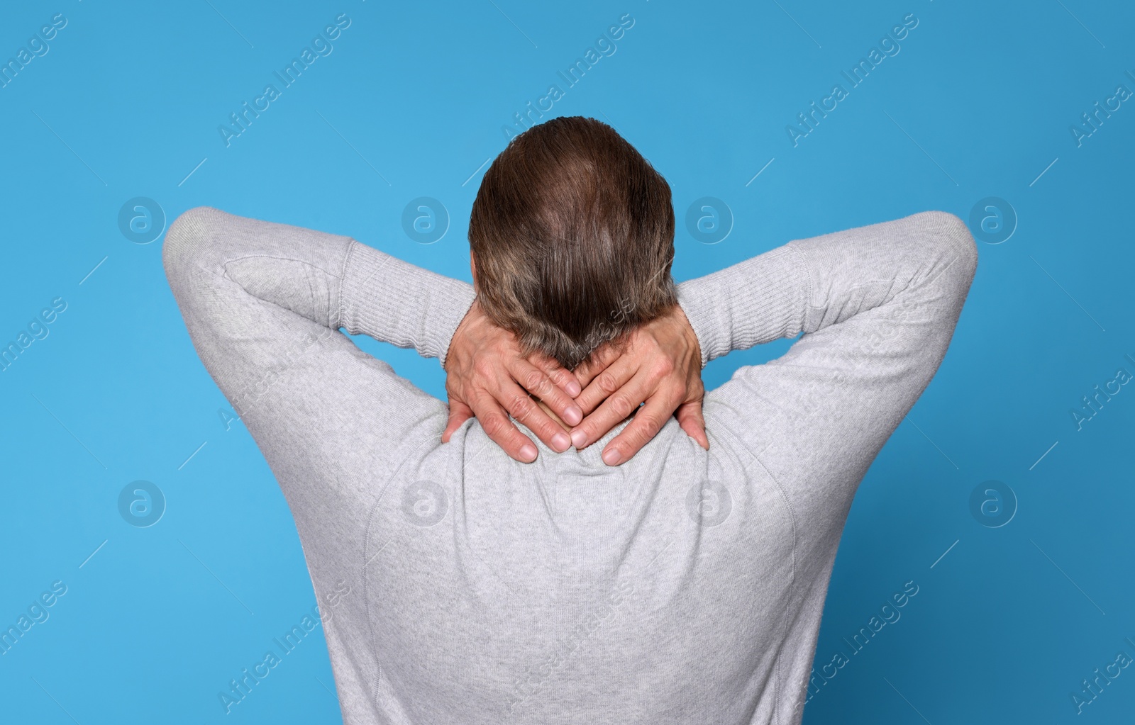 Photo of Senior man suffering from pain in back on light blue background. Arthritis symptoms