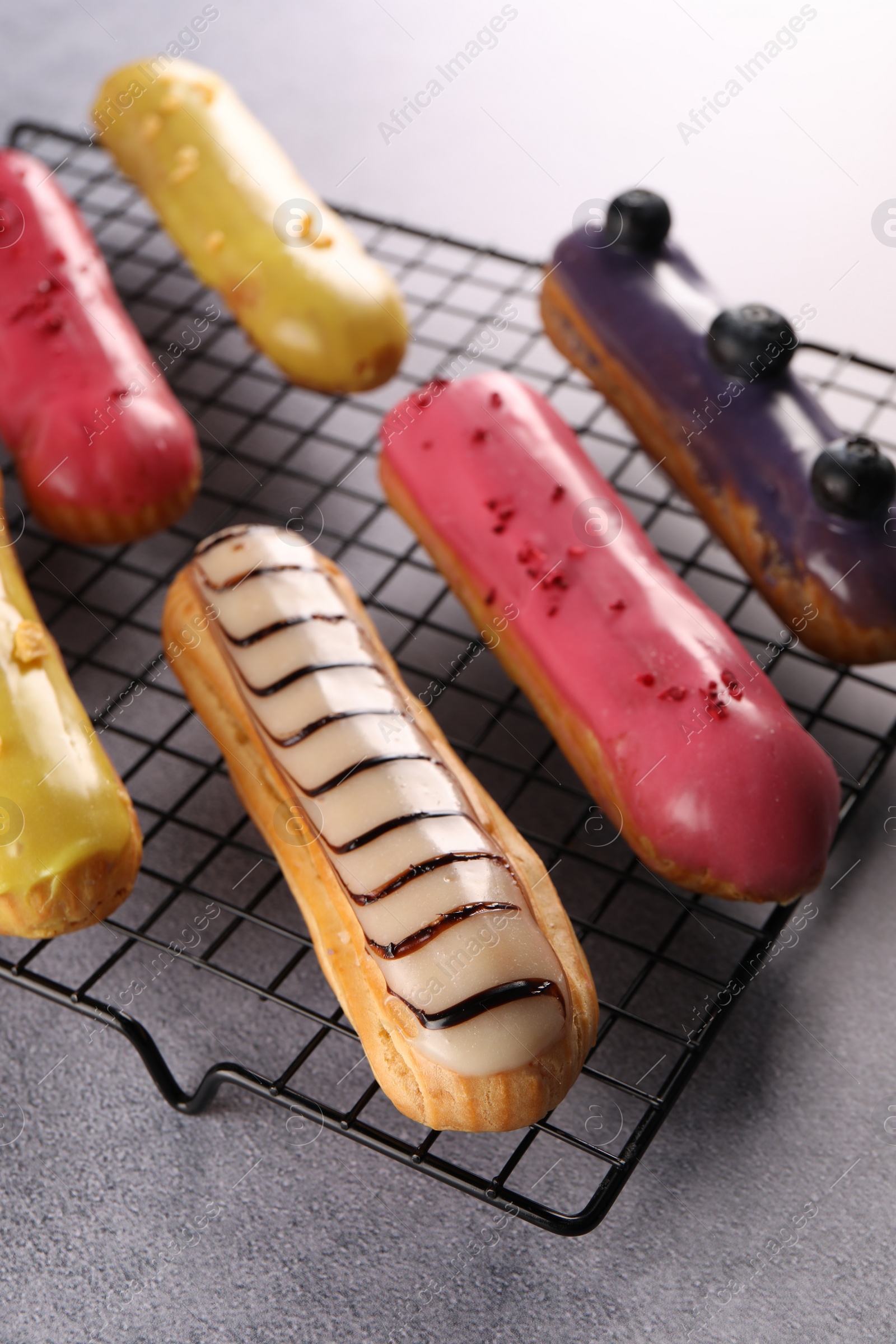 Photo of Cooling rack with different tasty glazed eclairs on grey table, closeup