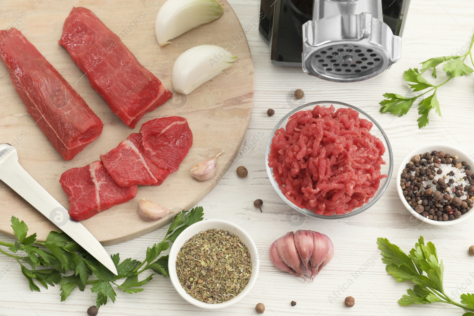 Photo of Meat grinder, beef, onion, garlic, parsley and spices on white wooden table, flat lay