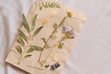 Photo of Sheet of paper with dried flowers and leaves on white fabric, top view