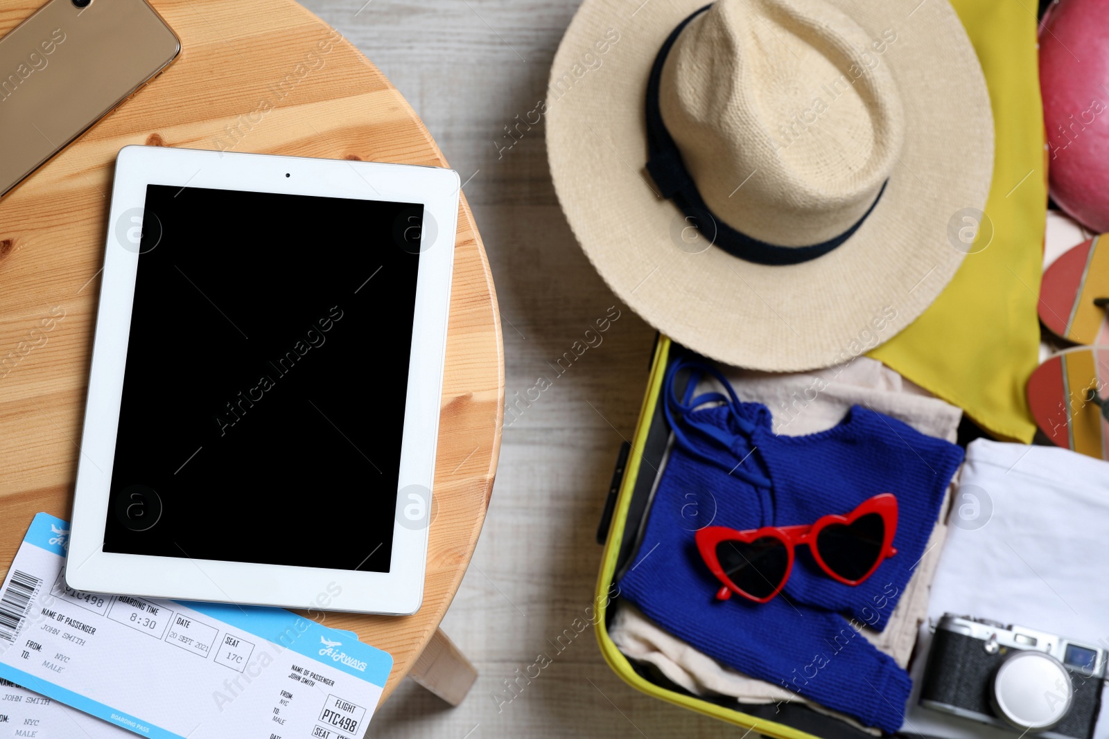 Photo of Modern tablet, tickets and smartphone on wooden table near packed suitcase, top view. Summer vacation