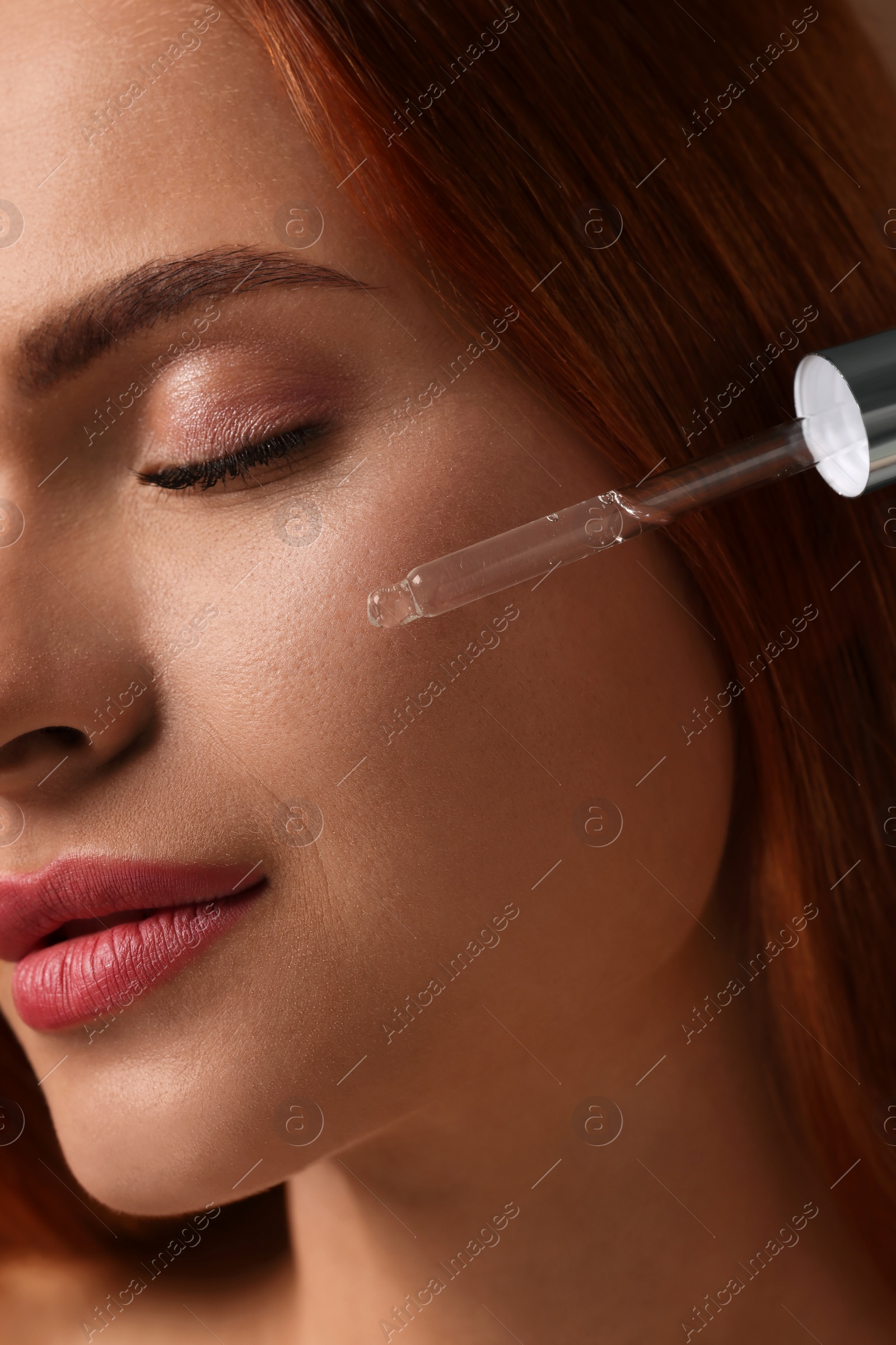 Photo of Beautiful young woman applying cosmetic serum onto her face, closeup