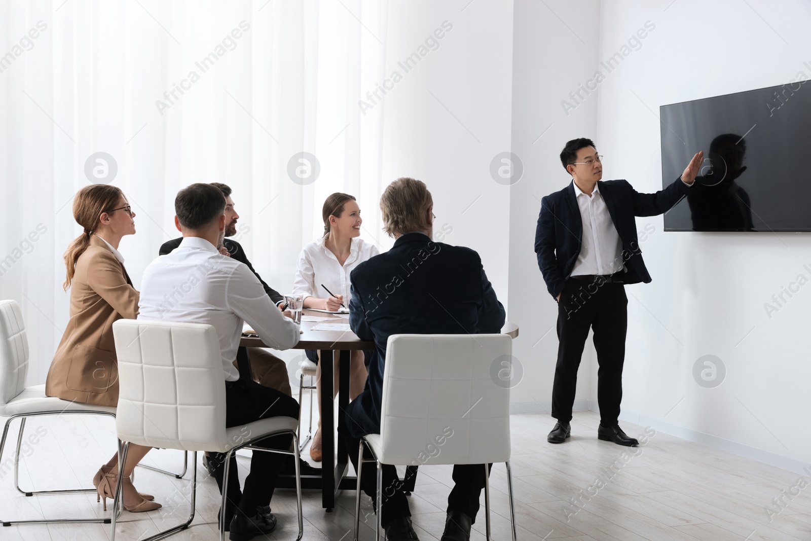 Photo of Business conference. Group of people listening to speaker report near tv screen in meeting room