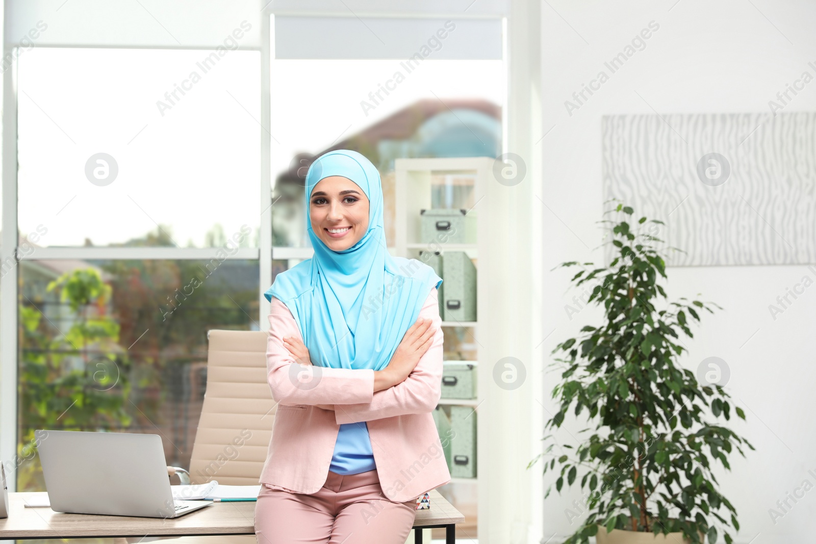 Photo of Modern Muslim businesswoman wearing hijab near table in light office