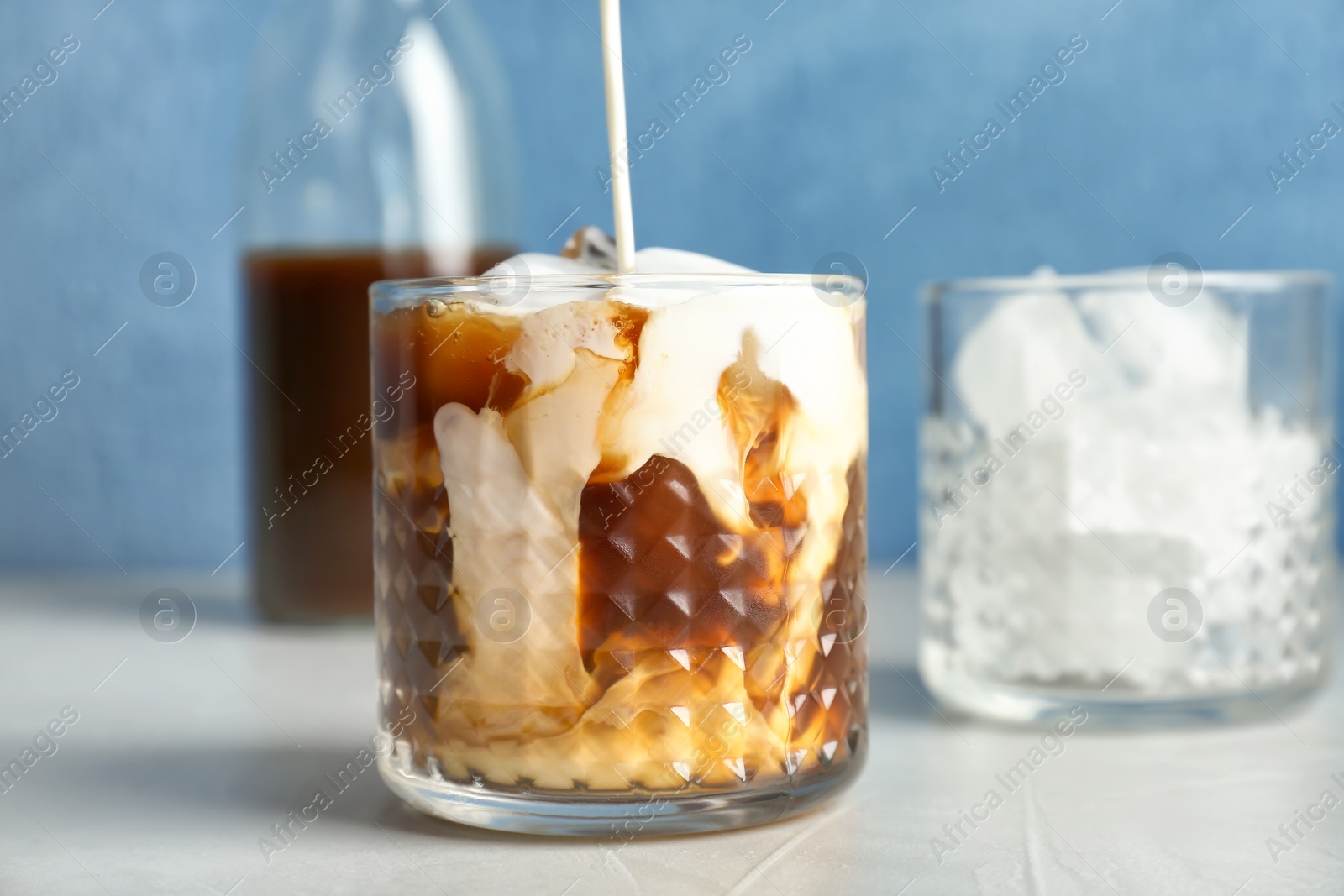 Photo of Pouring milk into glass with cold brew coffee on table