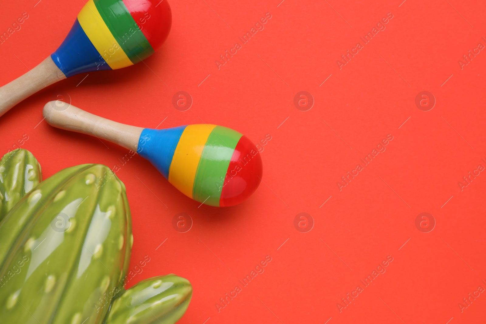 Photo of Colorful maracas and toy cactus on red background, flat lay with space for text. Musical instrument