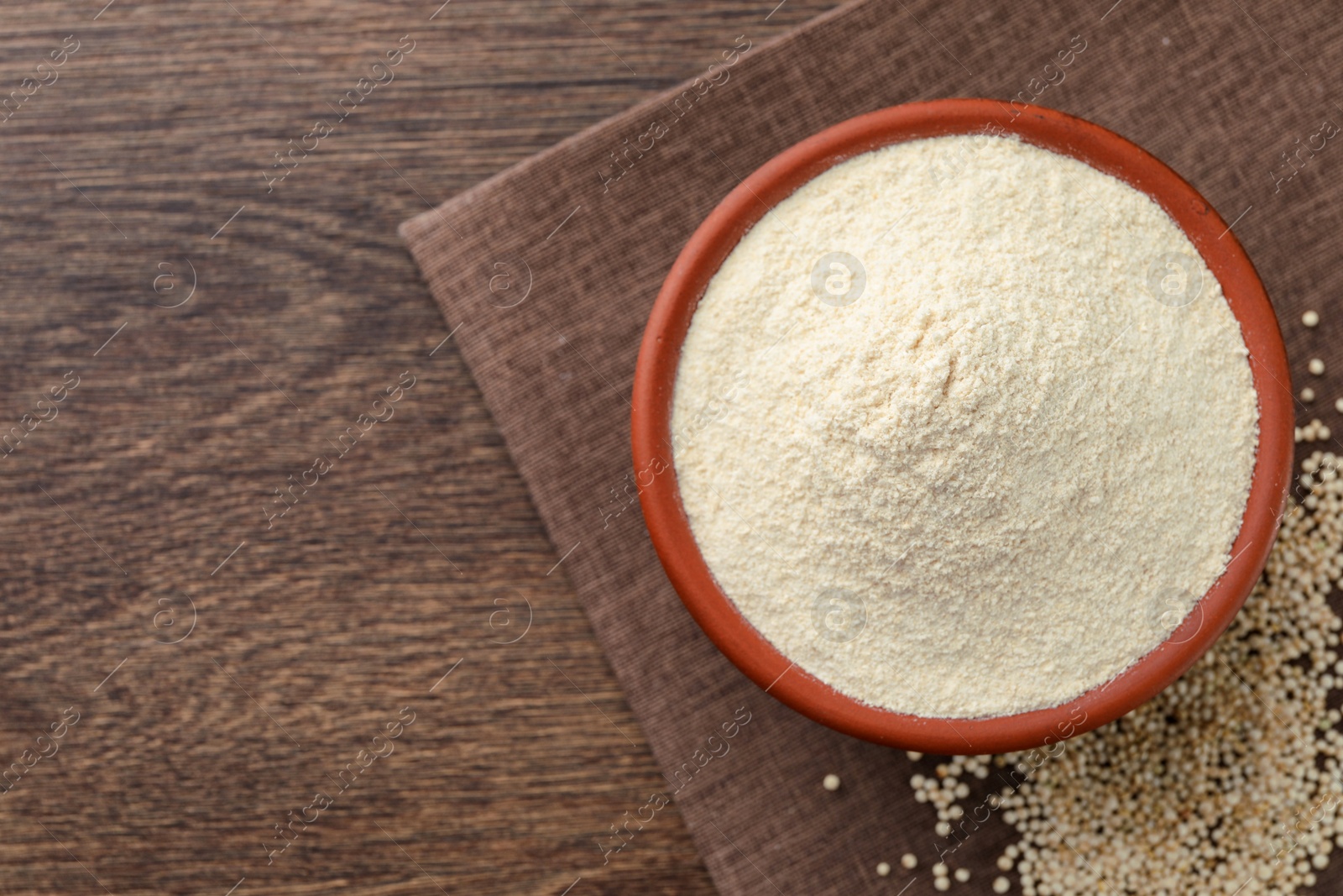 Photo of Quinoa flour in bowl and seeds on wooden table, top view. Space for text