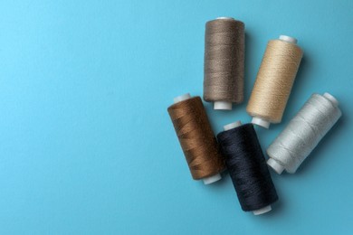 Photo of Different colorful sewing threads on light blue background, flat lay. Space for text