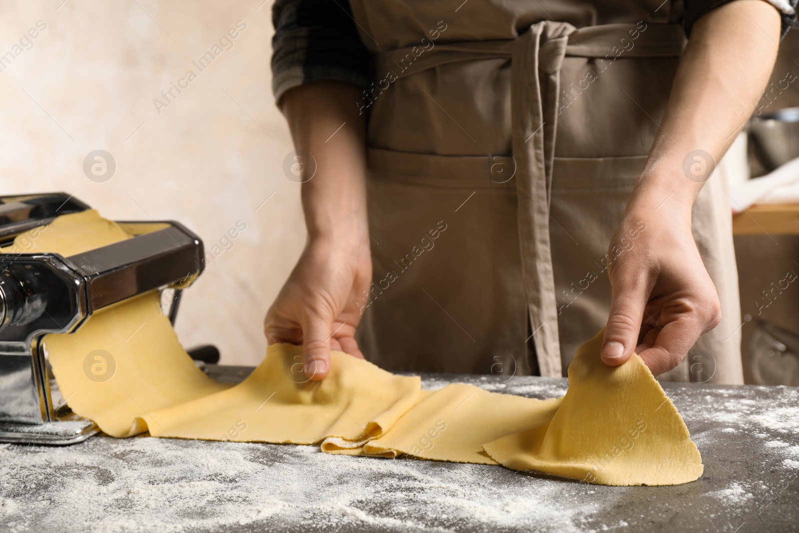 Photo of Woman preparing dough with pasta maker machine at grey table, closeup