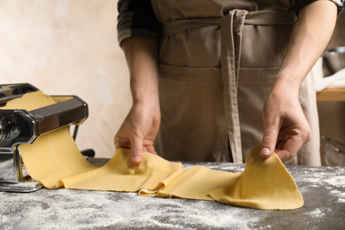 Woman preparing dough with pasta maker machine at grey table, closeup