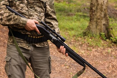 Photo of Man with hunting rifle wearing camouflage in forest, closeup