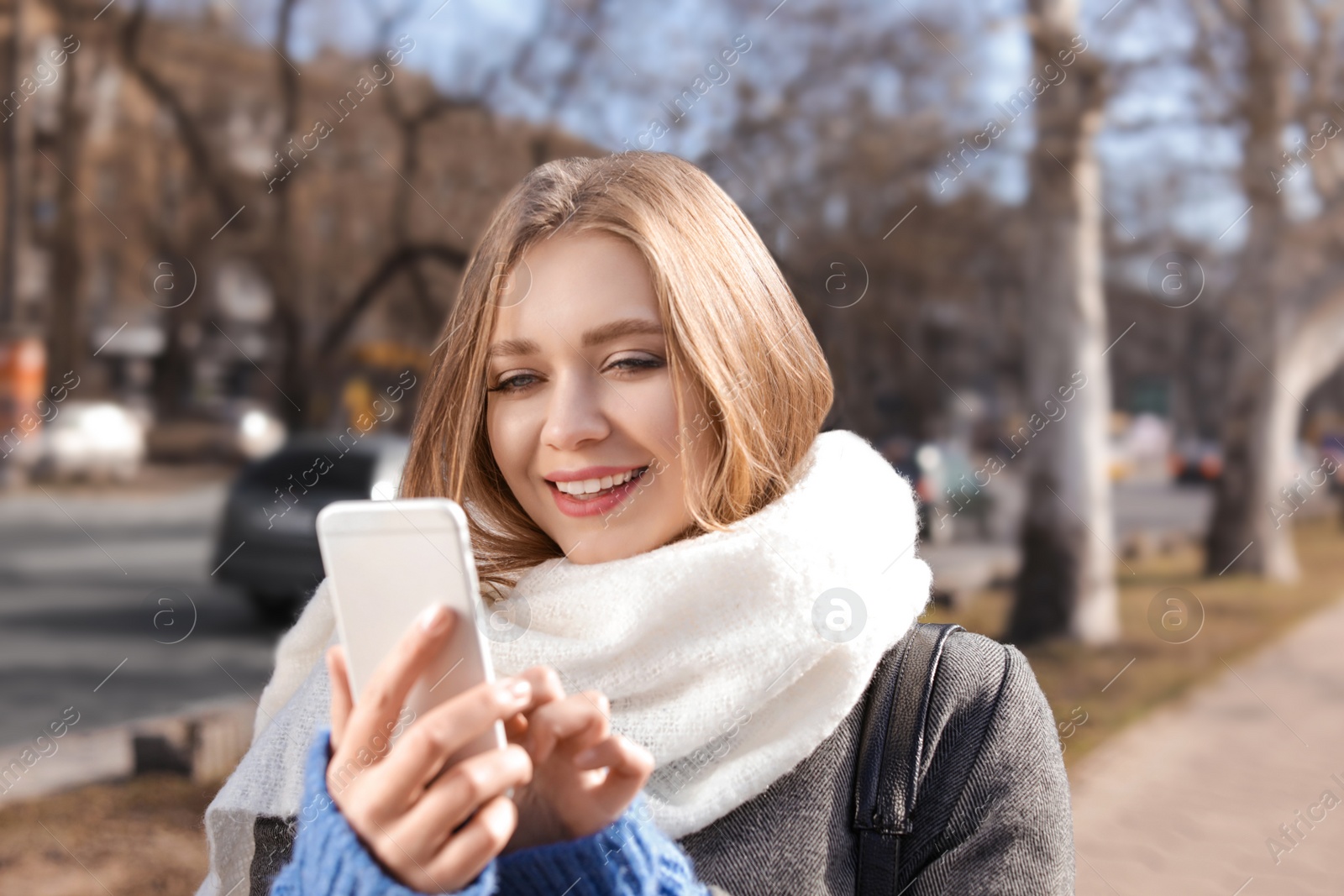 Photo of Portrait of happy young woman using phone outdoors on sunny day