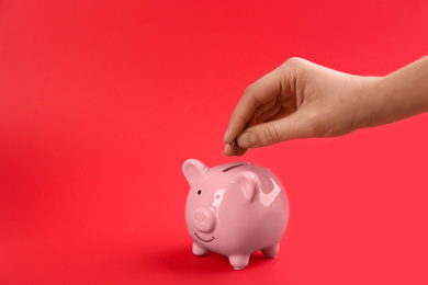 Photo of Woman putting coin into piggy bank on red background, closeup. Space for text