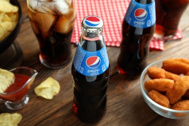 Photo of MYKOLAIV, UKRAINE - FEBRUARY 16, 2021: Glass bottles of Pepsi and snacks on wooden table