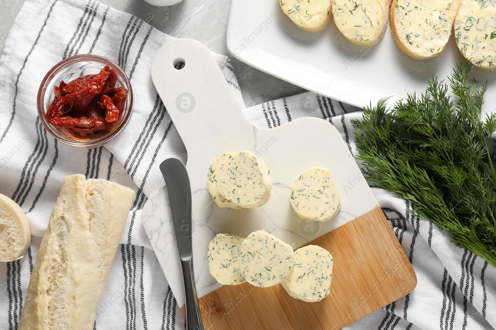 Photo of Tasty butter with dill, chili peppers, bread and knife on grey marble table, top view