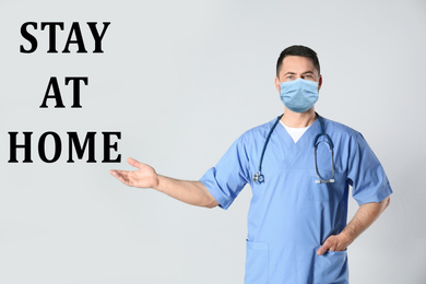 Doctor in medical mask and text STAY AT HOME on light background