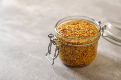 Jar of delicious whole grain mustard on grey table, space for text