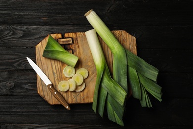 Photo of Fresh raw leeks on black wooden table, flat lay. Ripe onion
