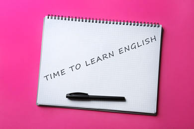 Image of Open notebook with text Time To Learn English and pen on pink background, top view