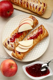 Fresh tasty puff pastry with jam and apples served on white textured table, flat lay
