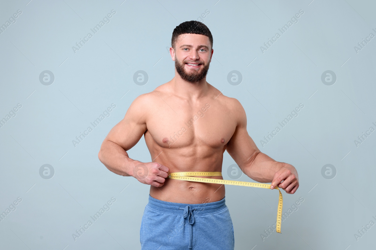 Photo of Portrait of happy athletic man measuring waist with tape on light grey background. Weight loss concept