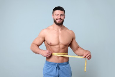 Photo of Portrait of happy athletic man measuring waist with tape on light grey background. Weight loss concept