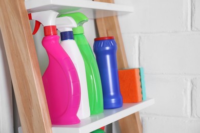 Photo of Different detergents and sponges on shelf near white wall indoors
