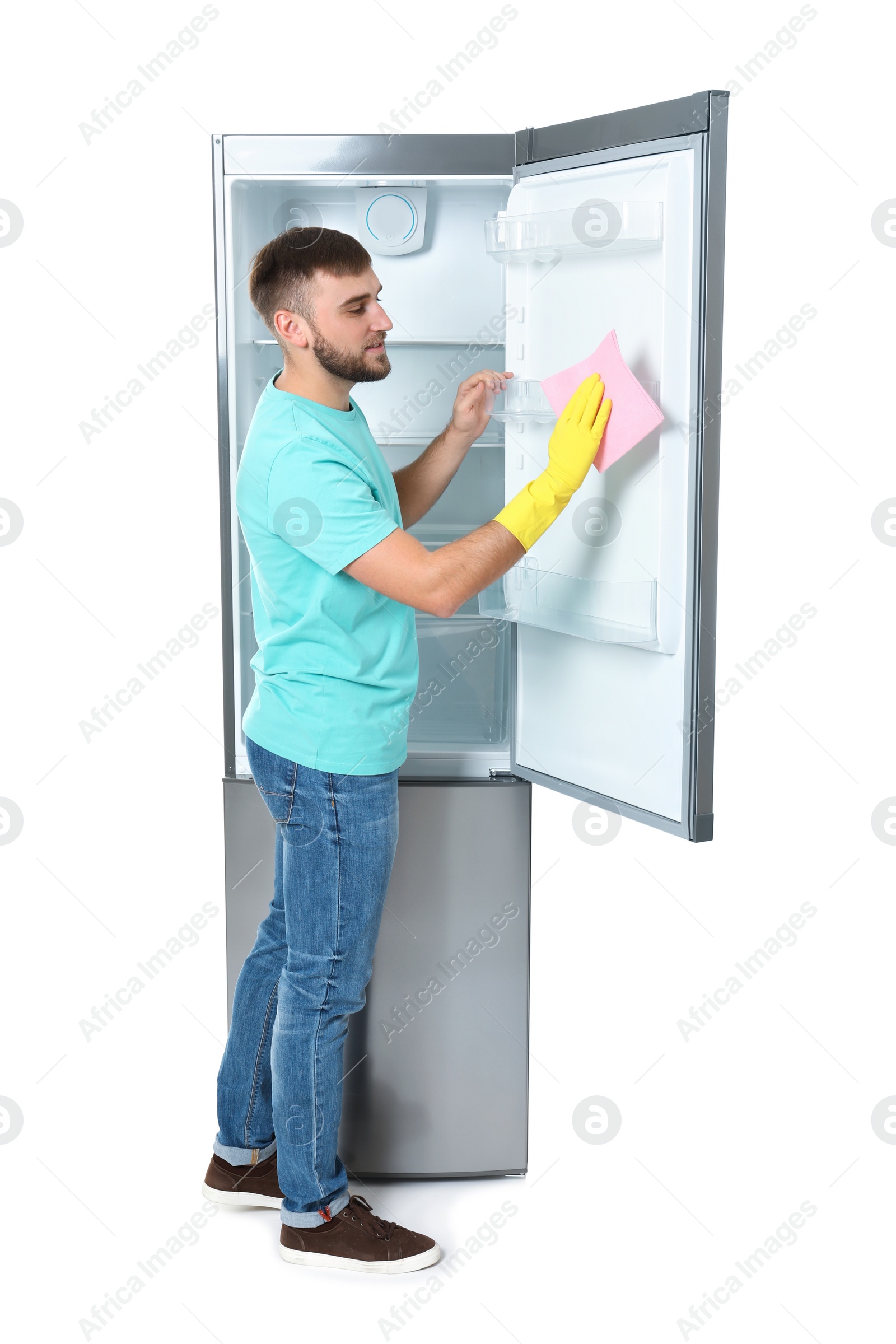 Photo of Young man cleaning refrigerator with rag on white background