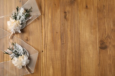 Photo of Stylish boutonnieres and ribbon on wooden table, top view. Space for text