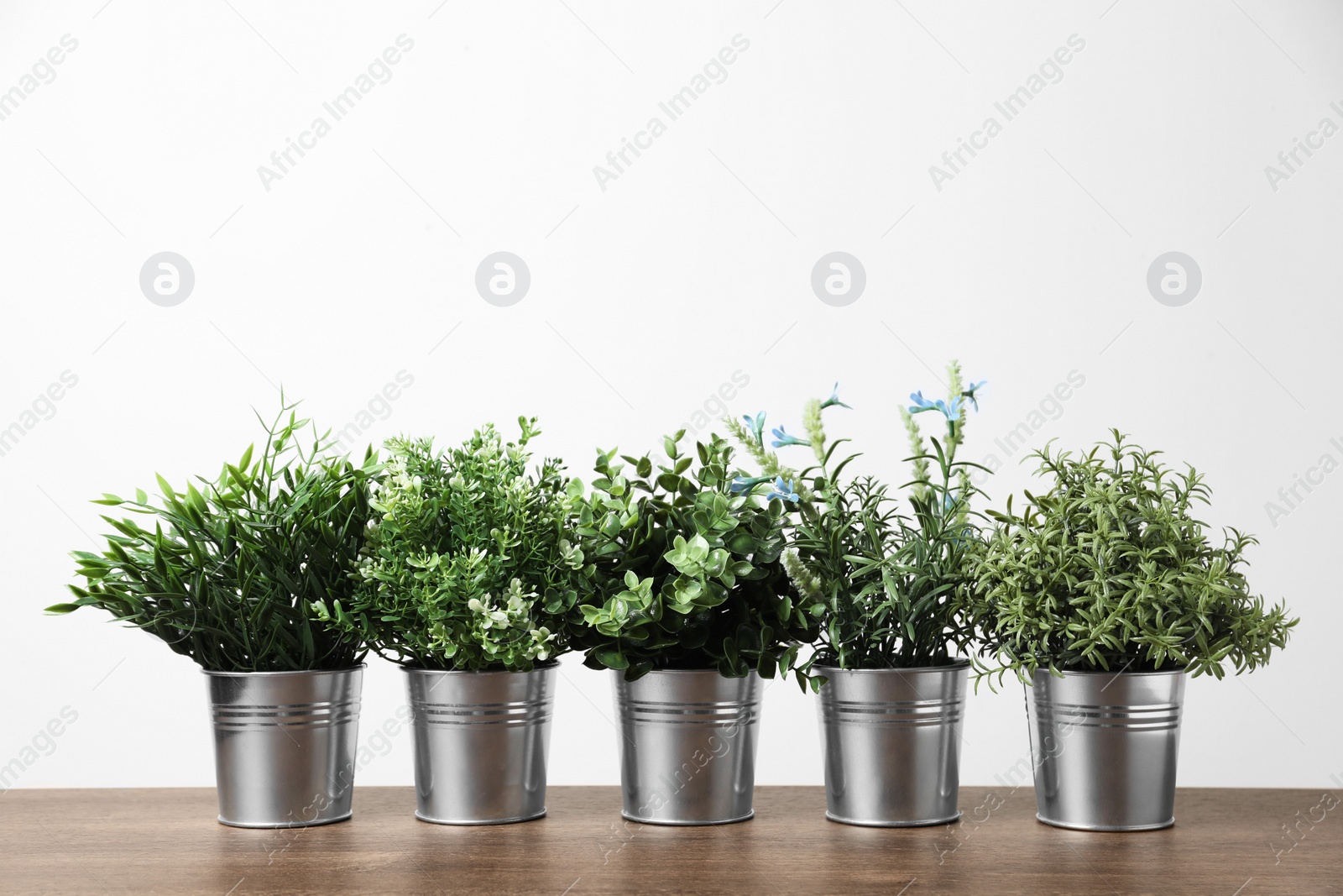 Photo of Different artificial potted herbs on wooden table against white background