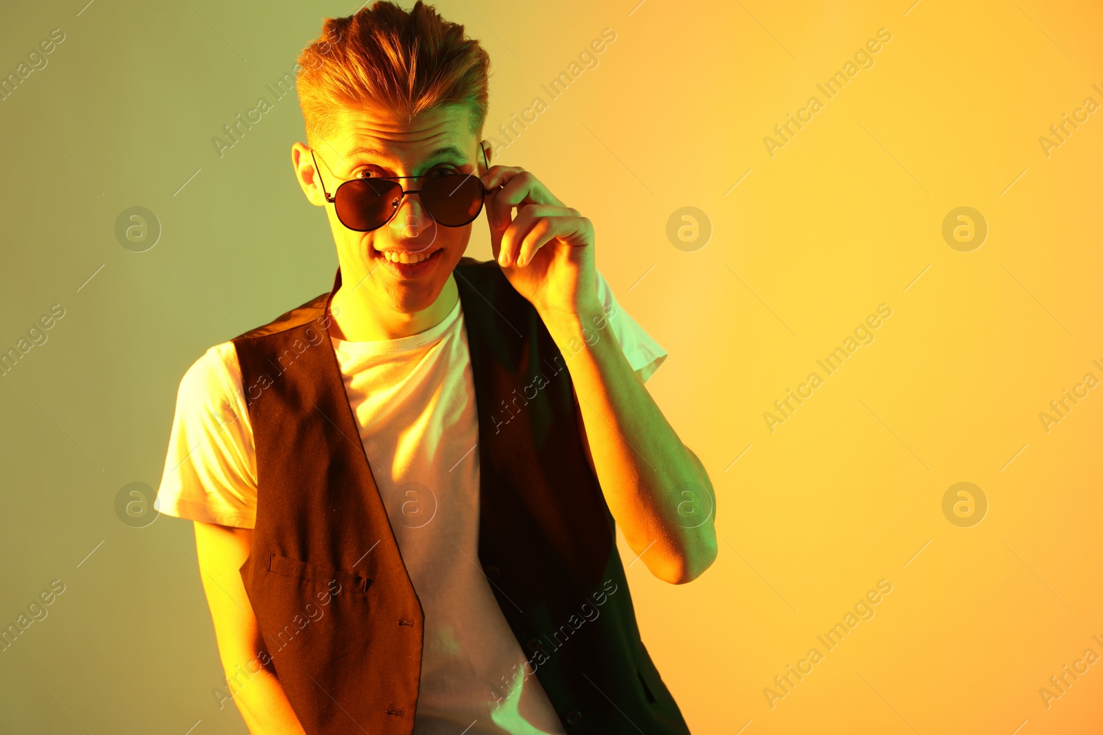 Photo of Stylish young man in sunglasses on color background in neon lights. Space for text