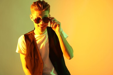 Photo of Stylish young man in sunglasses on color background in neon lights. Space for text