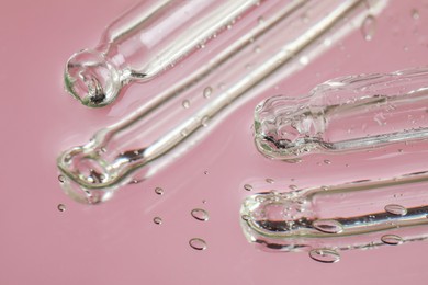Pipettes near serum drops on beautiful mirror, closeup. Toned in pink