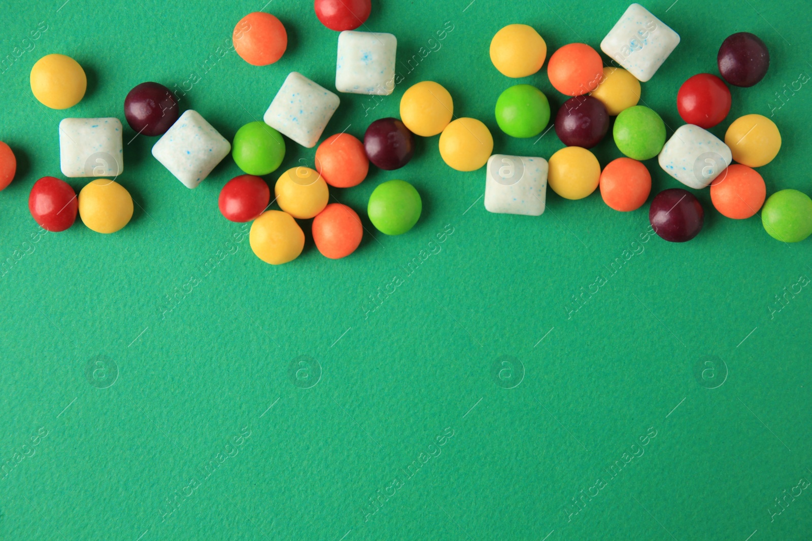 Photo of Different tasty chewing gums on green background, flat lay. Space for text