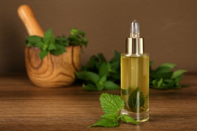 Photo of Glass bottle of nettle oil with dropper and leaves on wooden table against brown background, space for text