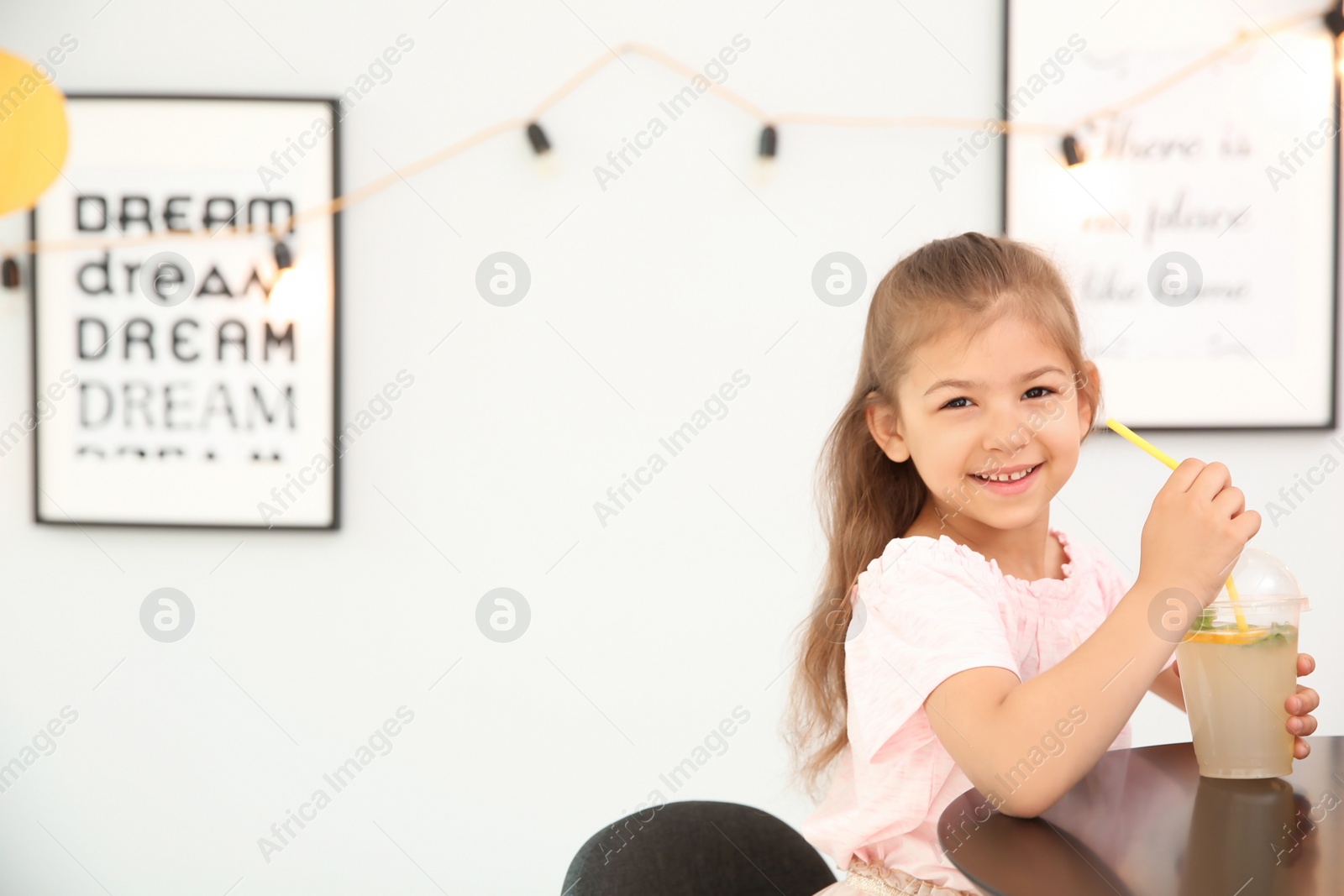 Photo of Little girl with natural lemonade at table indoors