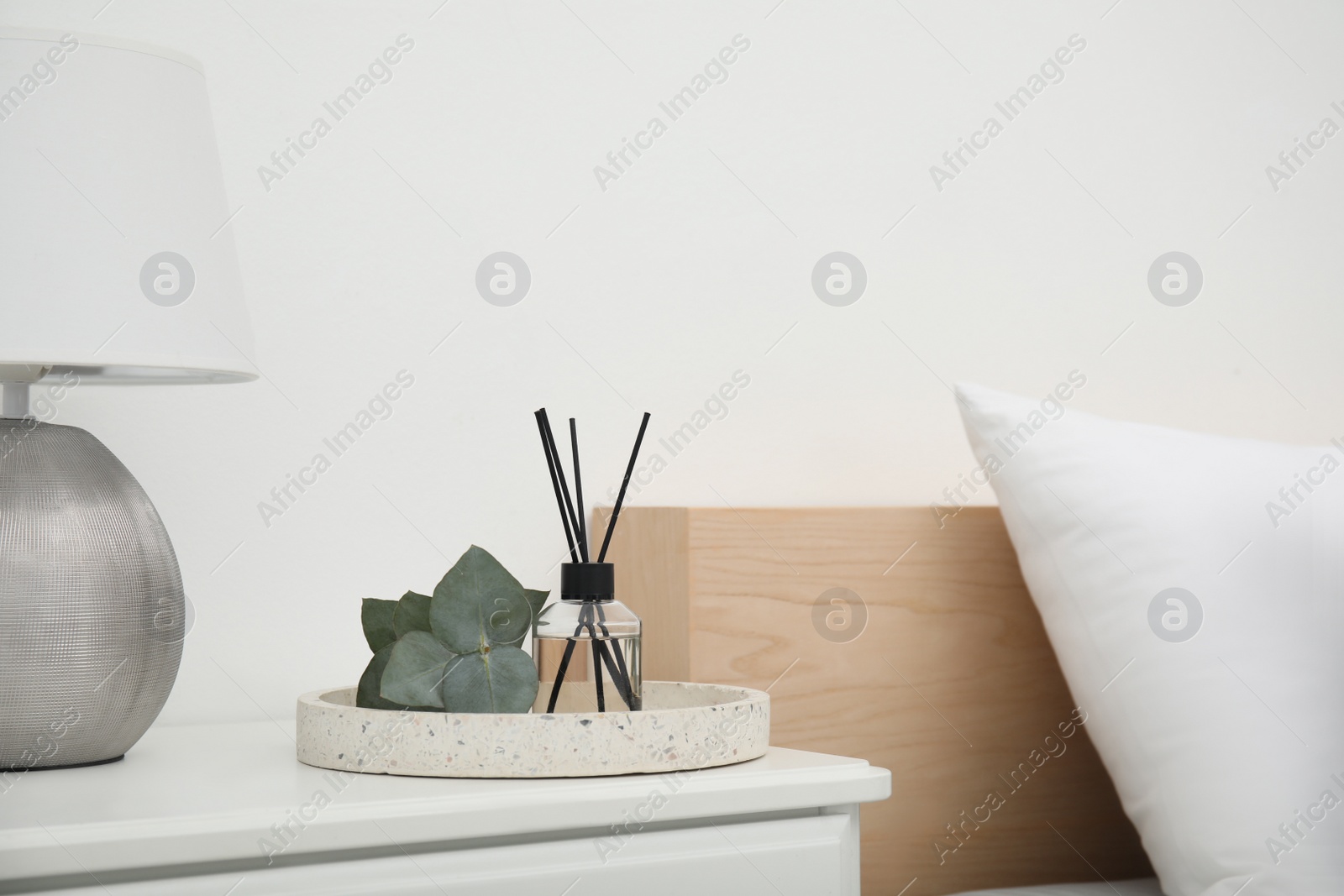 Photo of Reed diffuser with lamp and eucalyptus on nightstand in bedroom