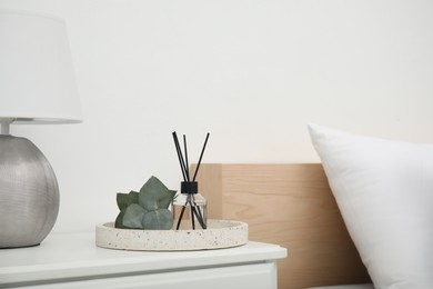 Reed diffuser with lamp and eucalyptus on nightstand in bedroom